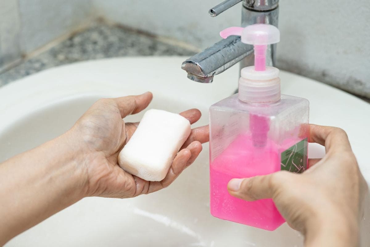 Hands holding bar and liquid soap by sink.
