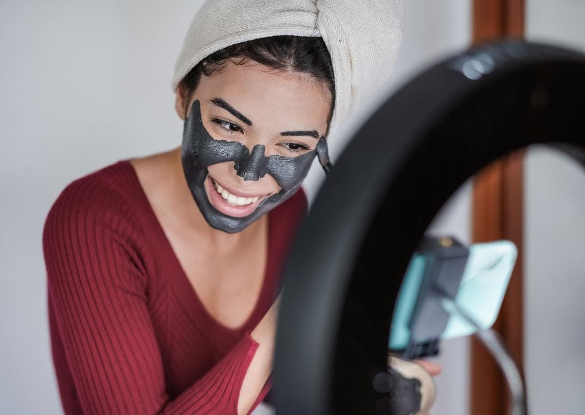 Woman applying charcoal face mask with mirror